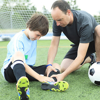 man helping a kid in soccer who hurt his ankle